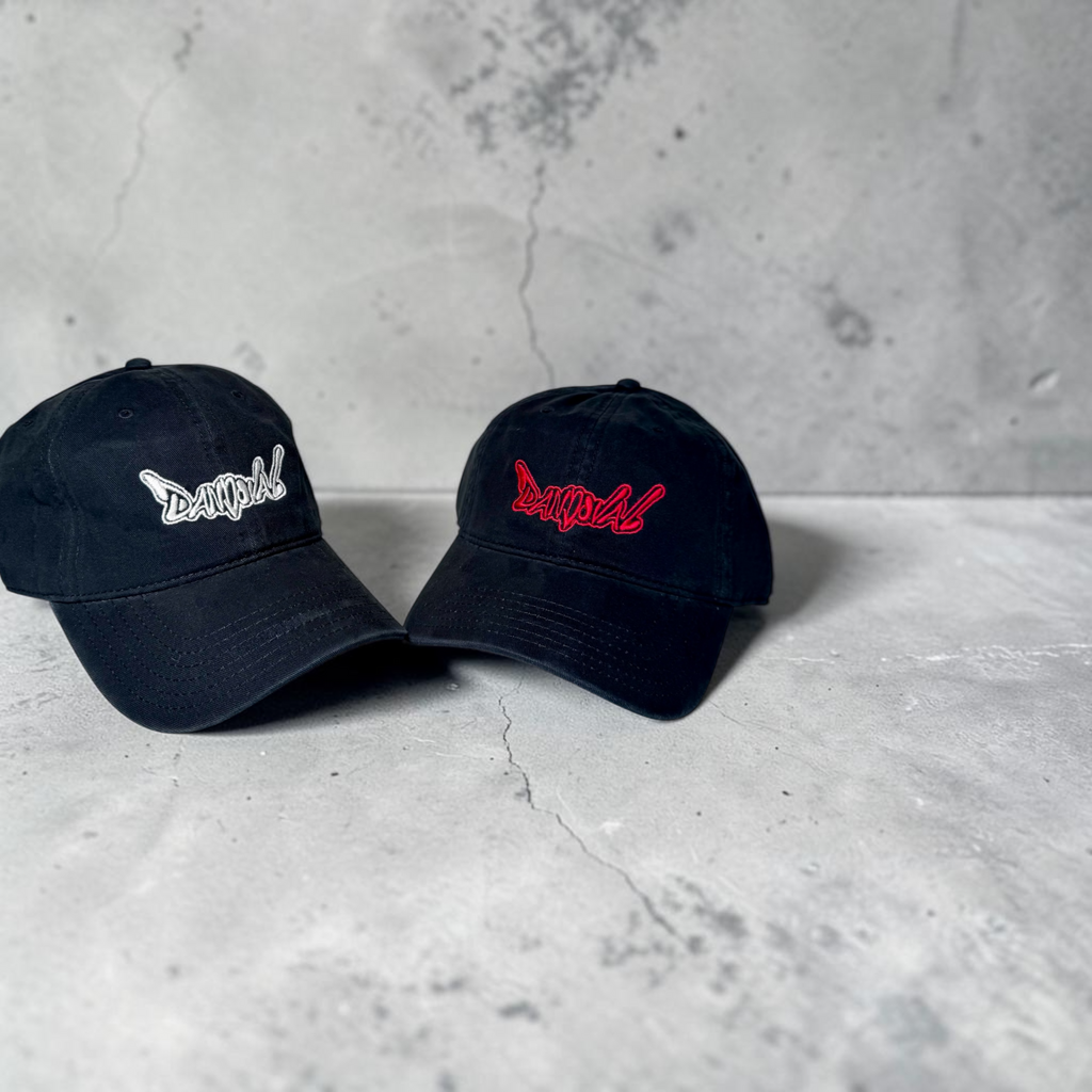 Two black baseball caps with embroidered logos on a concrete surface.