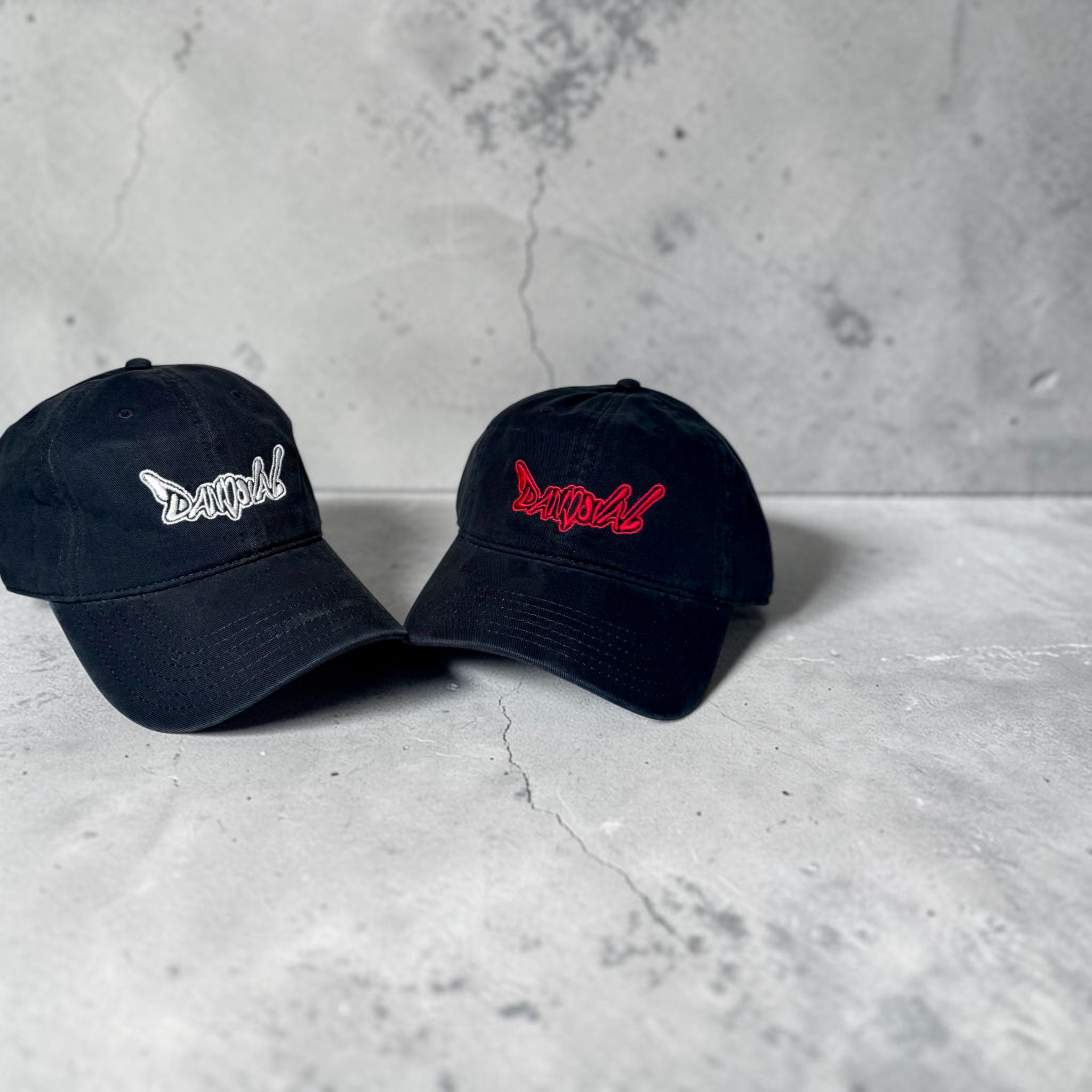 Two black baseball caps with embroidered logos on a concrete surface.