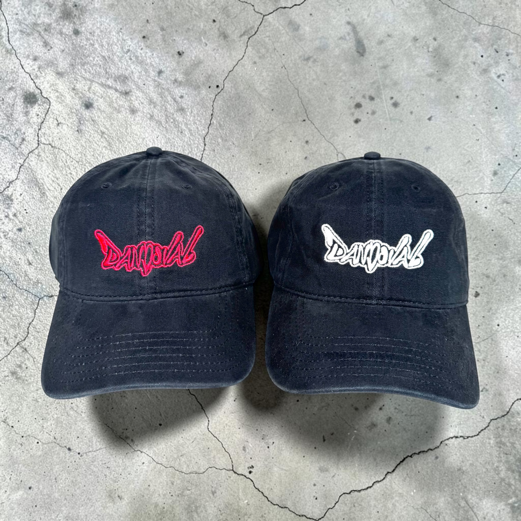 Two black baseball caps with red and white text on a concrete surface