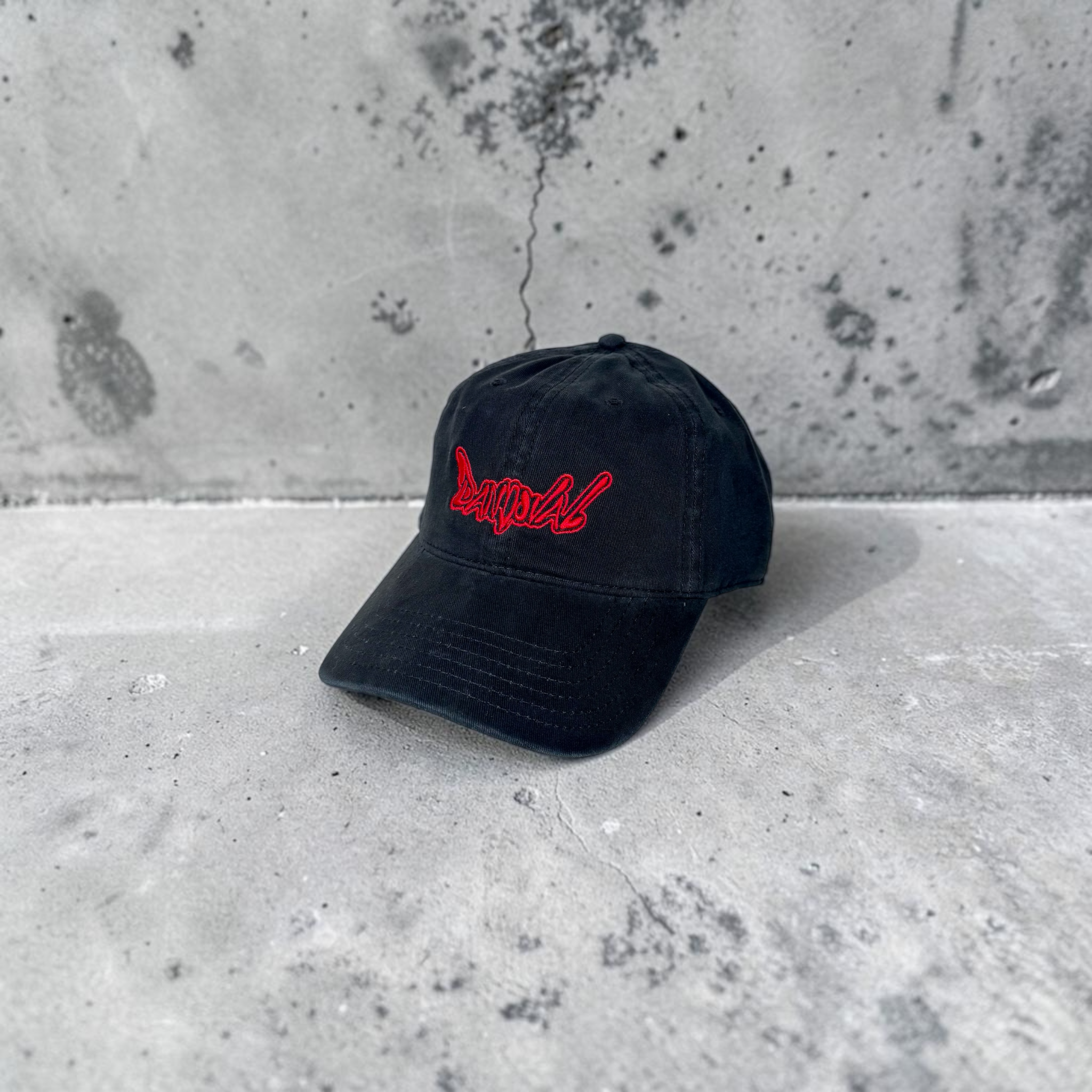 Black cap with red logo on a concrete surface