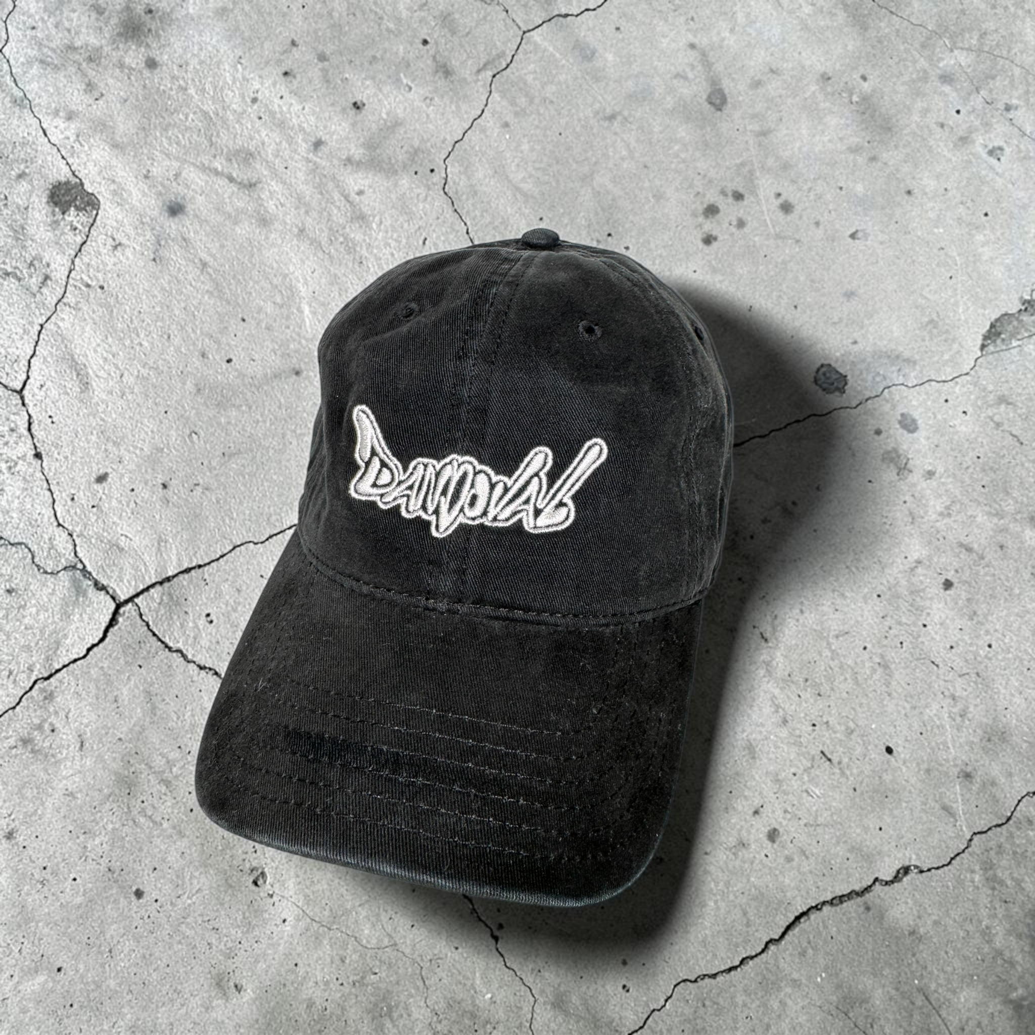 Black cap with white logo on a cracked concrete surface