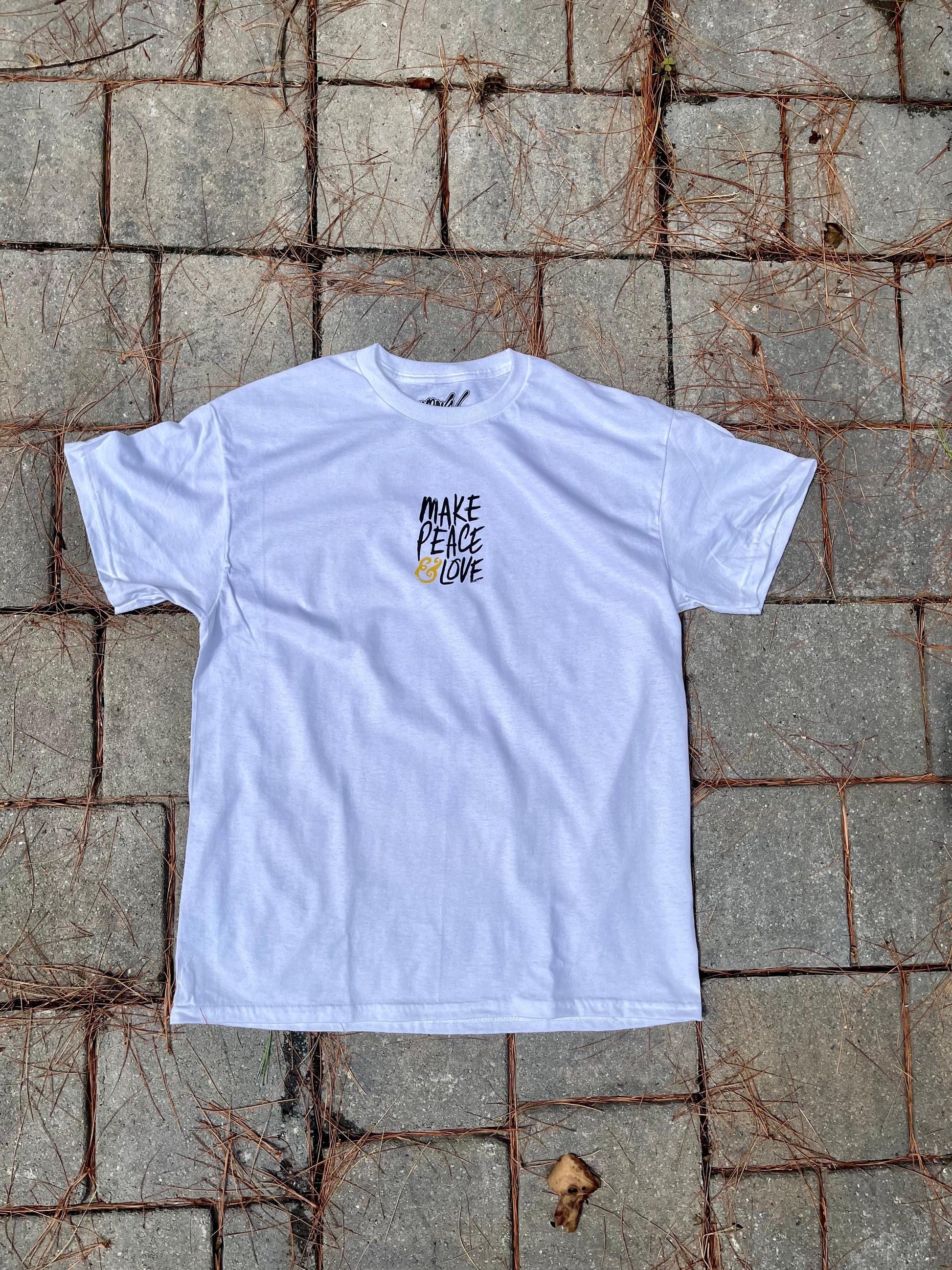 White t-shirt with 'Make Peace Love' text on a textured stone surface