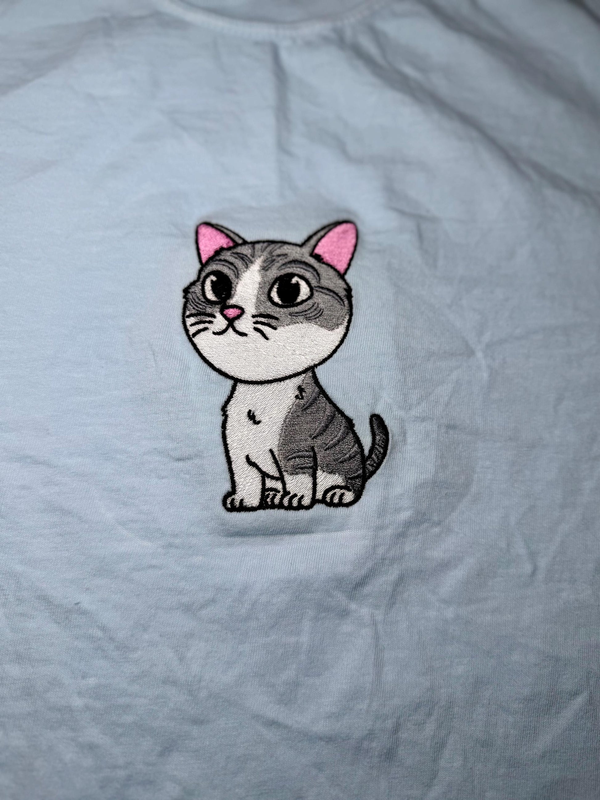 Embroidered cat patch on a light gray fabric background